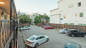 A parking lot with several cars, a building with a white facade, and a fenced area with trees. - Montrose Dazzle Studio, Near Med Center (Houston)