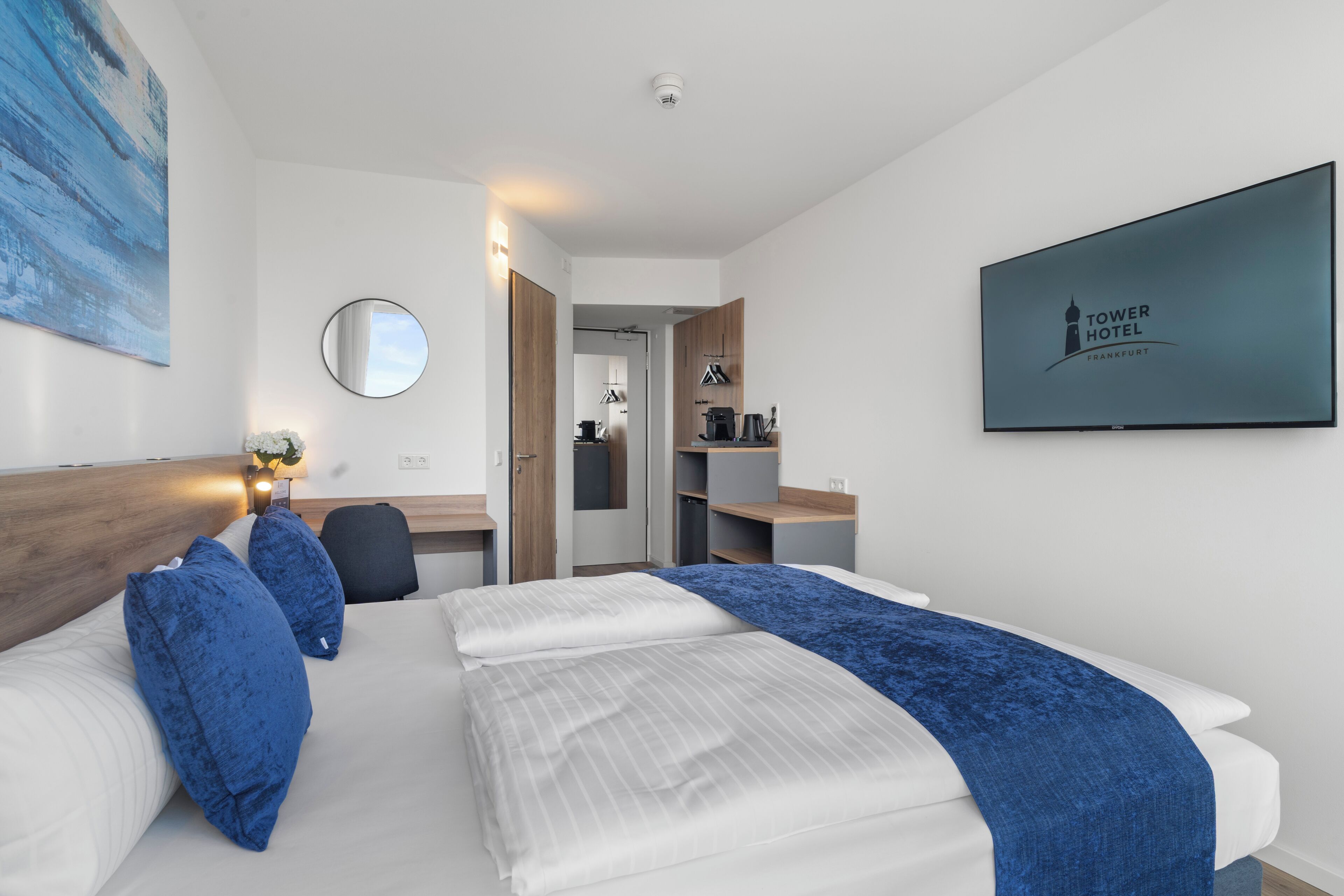 Une chambre d’hôtel comprenant un lit, un bureau, une chaise, un miroir, une télévision et une porte donnant accès à une salle de bain.