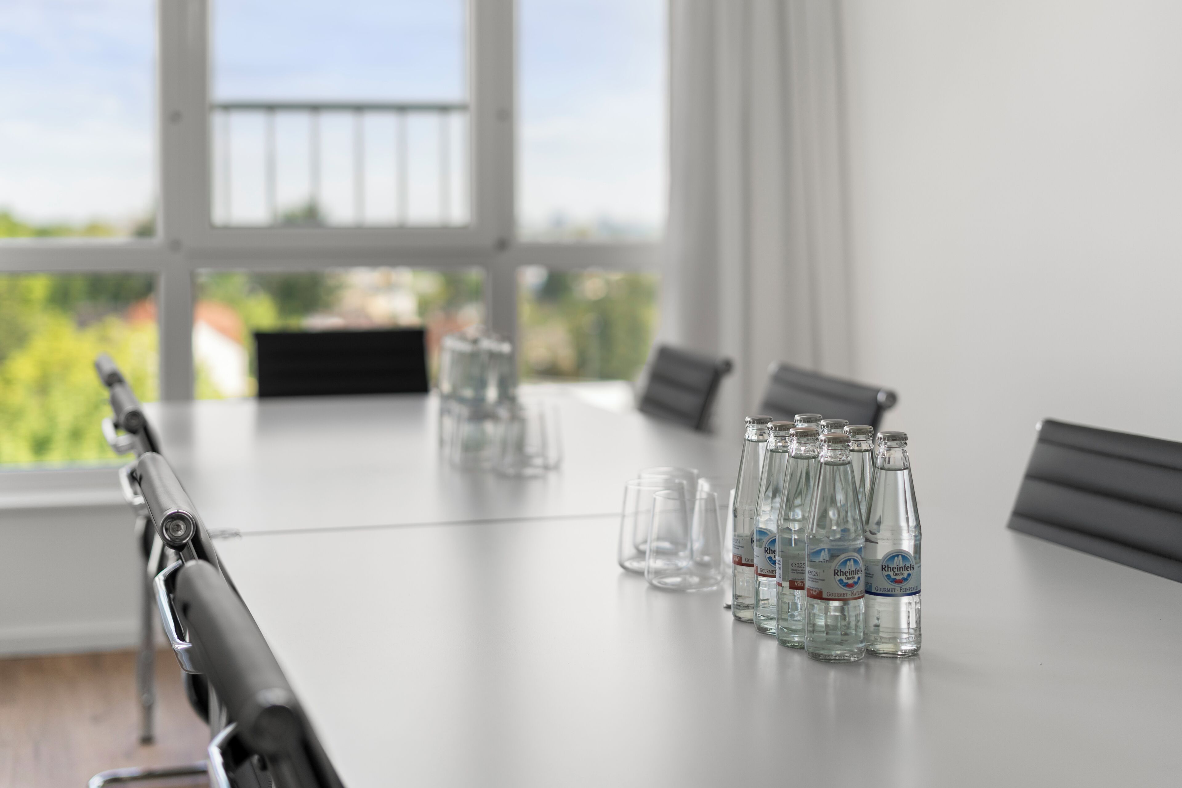 A conference table with chairs, clear glasses, and bottles of water.