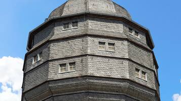A tower with a conical roof and a spire, featuring multiple windows and a brick base.