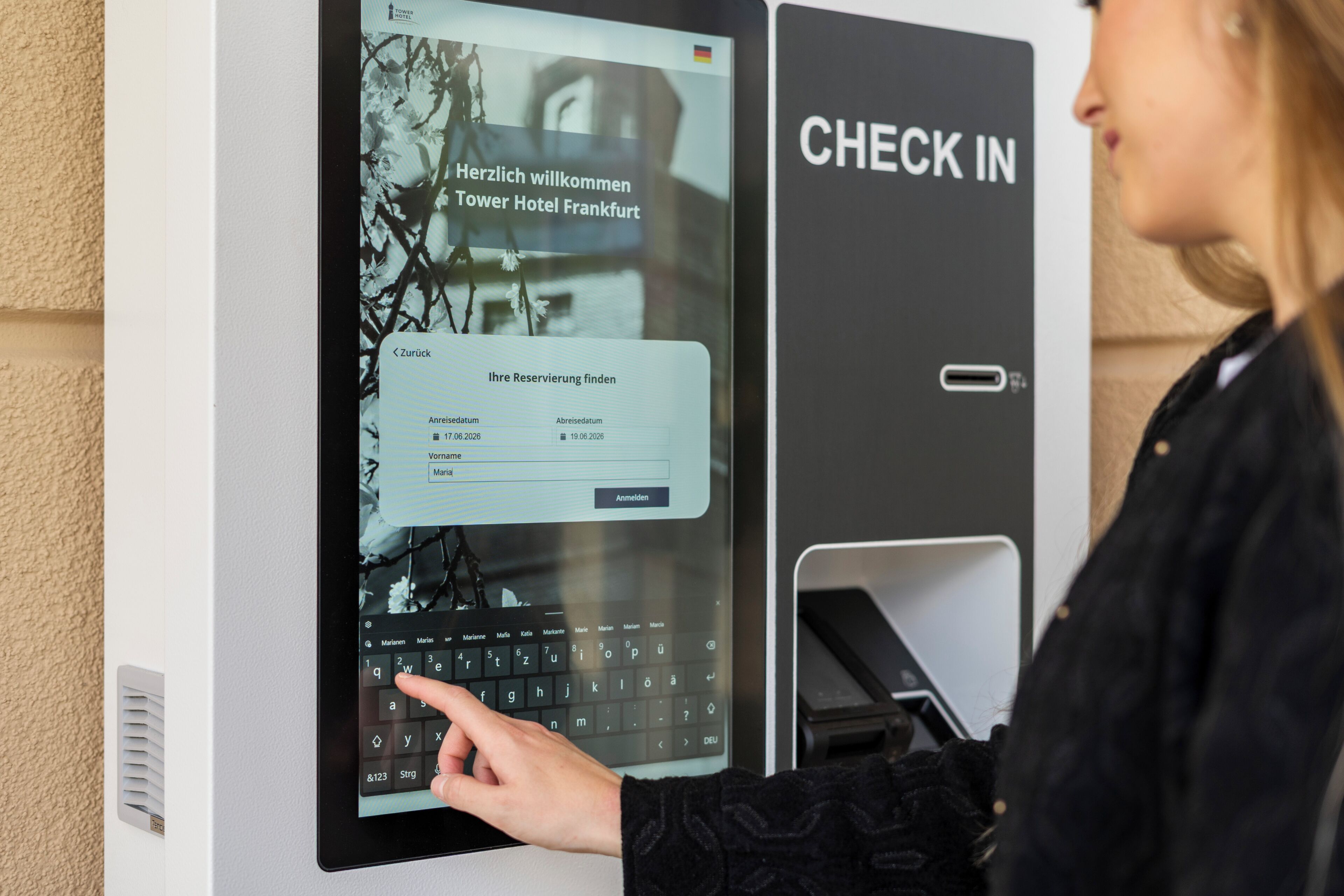 A digital kiosk with a 'CHECK IN' sign, a keyboard interface, and a screen displaying a welcome message for Tower Hotel Frankfurt.
