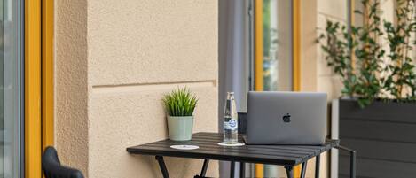An outdoor table with a laptop, a bottle of water, and a potted plant.