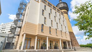 Un hotel de varios pisos con una llamativa escalera en espiral, una torre en forma de cúpula y un acceso cubierto con mesas al aire libre.