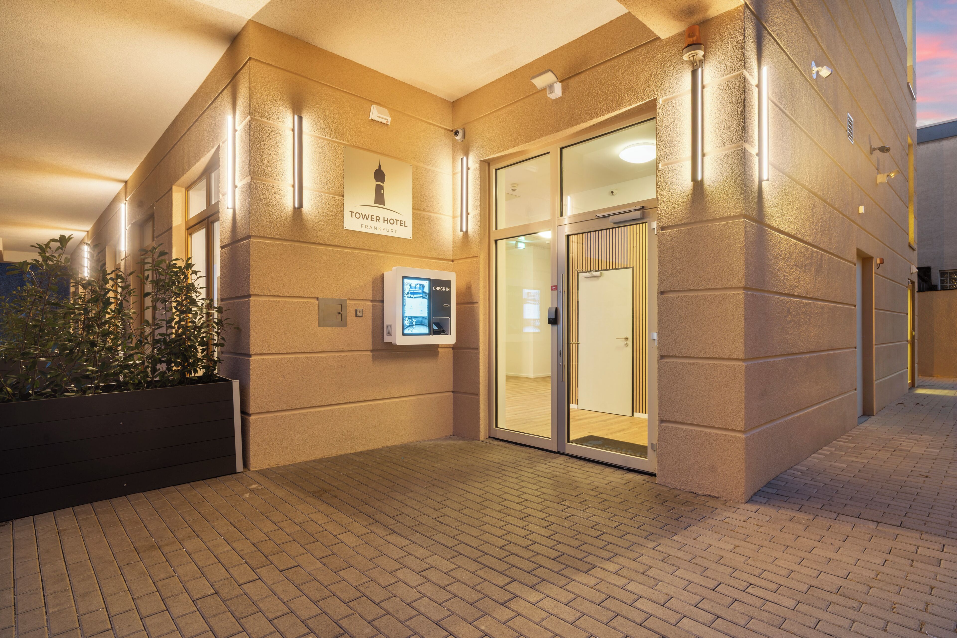 A hotel entrance with a check-in kiosk, a sign indicating the hotel name, and a door leading inside.