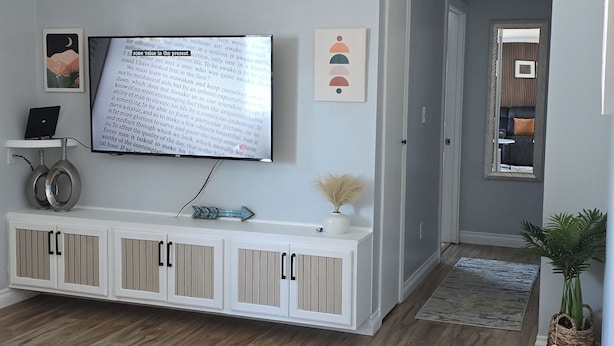 Ein Wohnzimmer mit Flachbildfernseher, einer weißen Unterhaltungsecke und Holzboden.