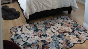 Ein Schlafzimmer mit einem Bett, Nachttischen, einem Wandbild und einem gemusterten Teppich.