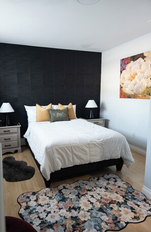 A bedroom with a bed, nightstands, a wall-mounted painting, and a patterned rug. - Near Airport cozy 2 bedroom  (Anchorage)