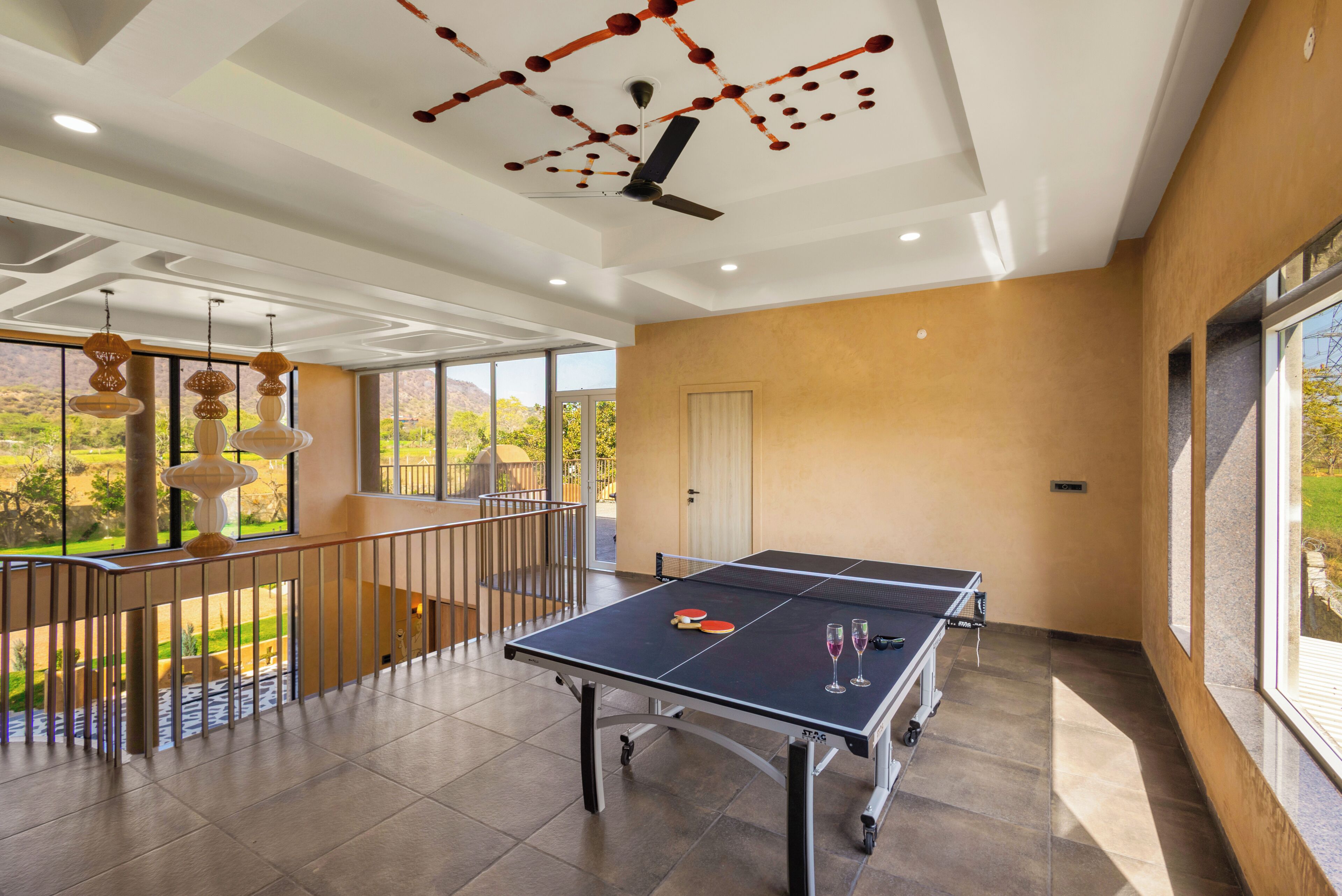 A ping pong table in a room with a balcony, large windows, and a ceiling with a unique design.