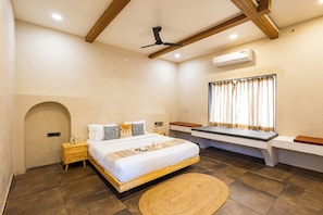 A bedroom with a bed, bedside tables, a window with curtains, a ceiling fan, and an air conditioning unit. - ELIVAAS Tuscan 5BHK Villa with Pvt Pool  (Pushkar)