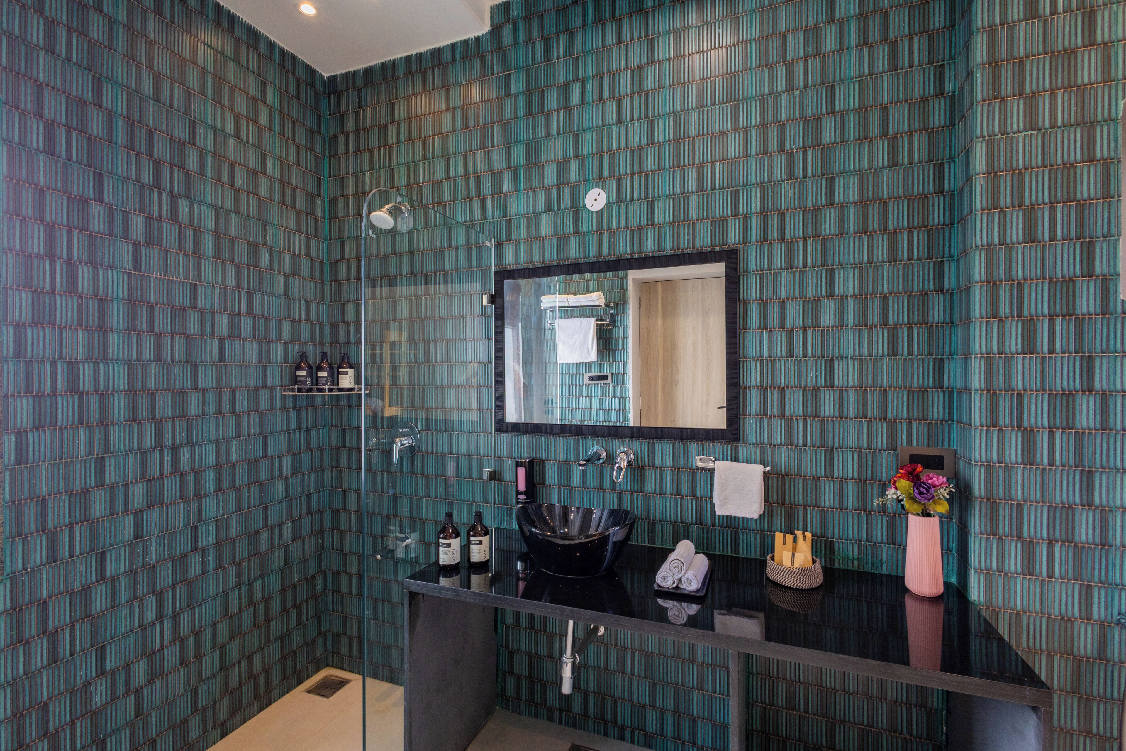 A bathroom with a glass shower enclosure, a black sink, and a mirror above it.
