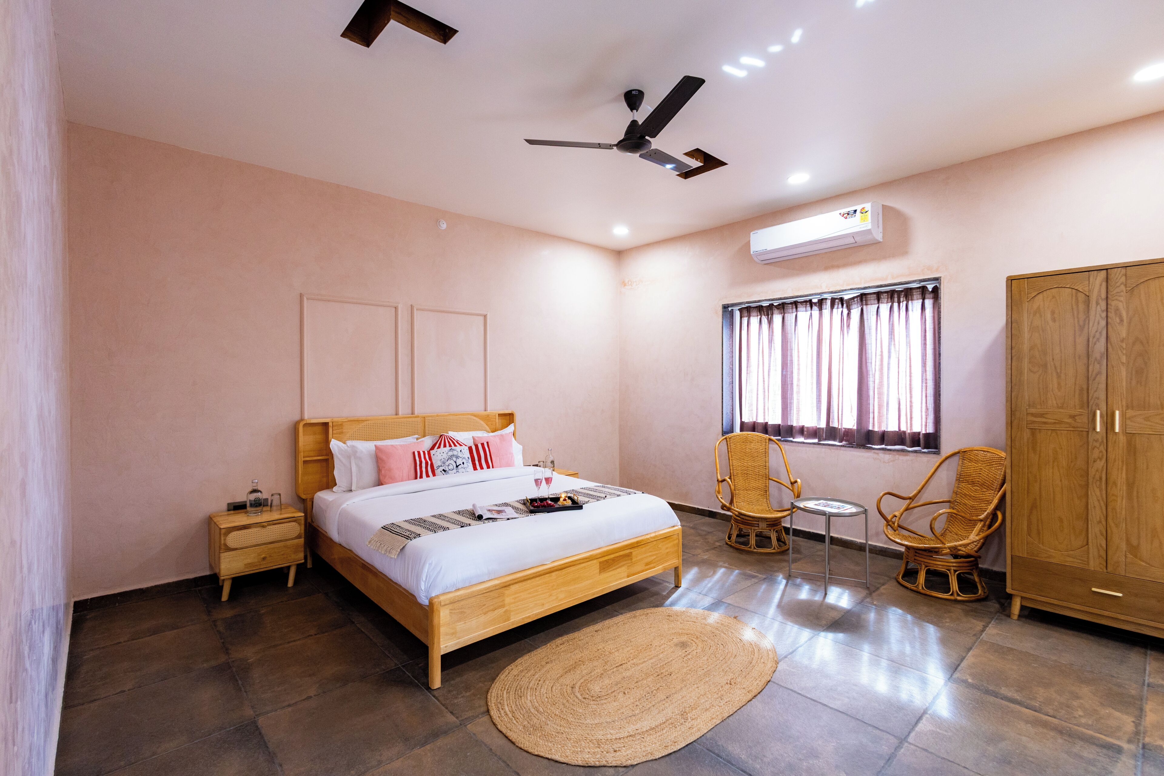 Una habitación de hotel con cama, mesita de noche, silla, armario, ventana con cortinas y ventilador de techo.