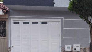 A garage with a large white door, a brown door with a decorative window, and a tree in front. - Beautiful house in Cartago Valle (Cartago)