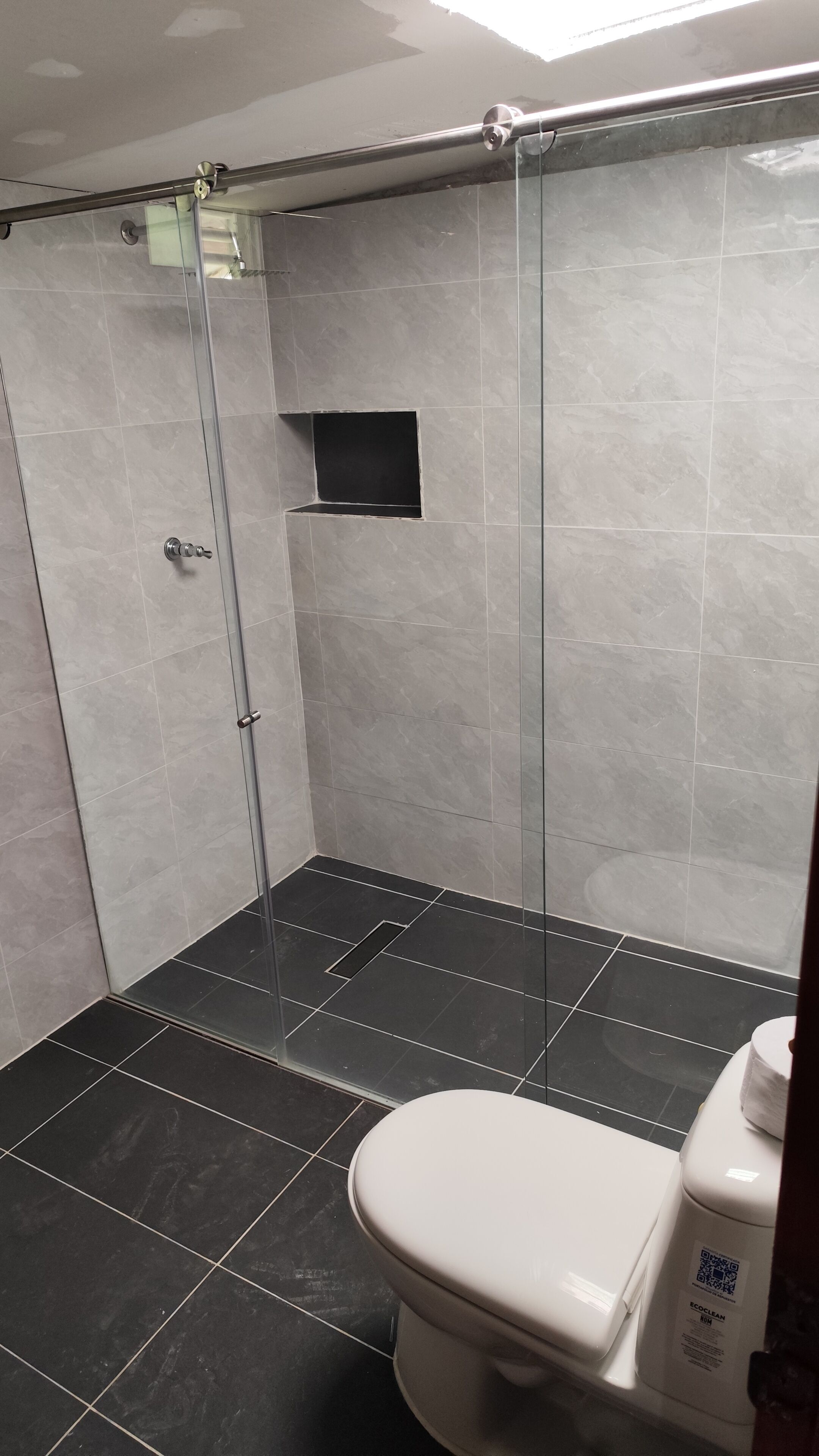 A bathroom with a glass-enclosed shower, a toilet, and a small shelf.