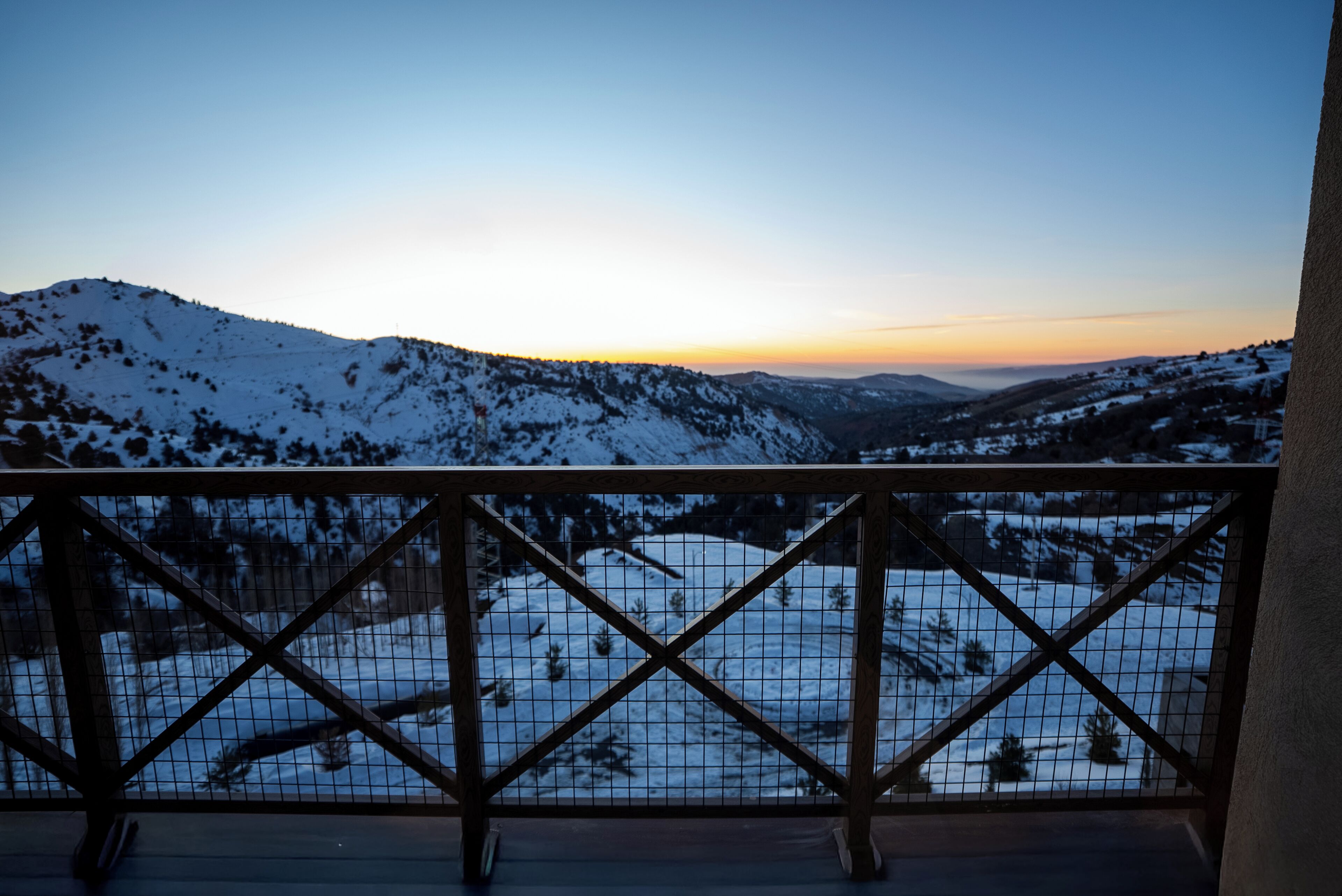A snow-covered landscape viewed through a wooden balcony railing.