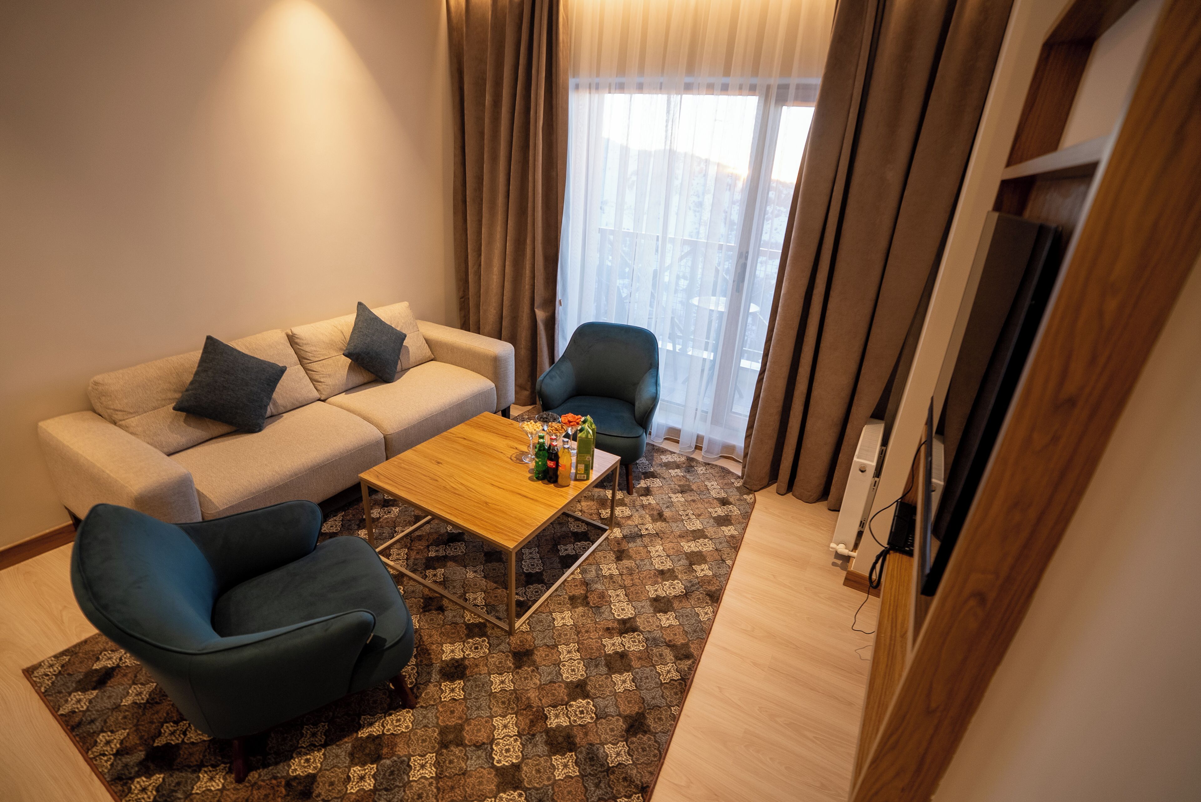 Ein modernes Wohnzimmer mit einer Couch, zwei Sesseln, einem Holztisch und einem gemusterten Teppich.