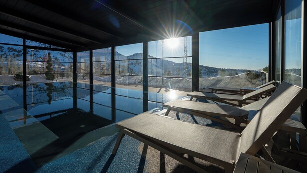 Un salón con paredes de vidrio y vistas soleadas a un paisaje montañoso.
