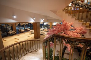 A hotel interior with a staircase, dining area, and artificial cherry blossom tree. - ZAFARON PREMIUM HOTEL  (Chimgan)