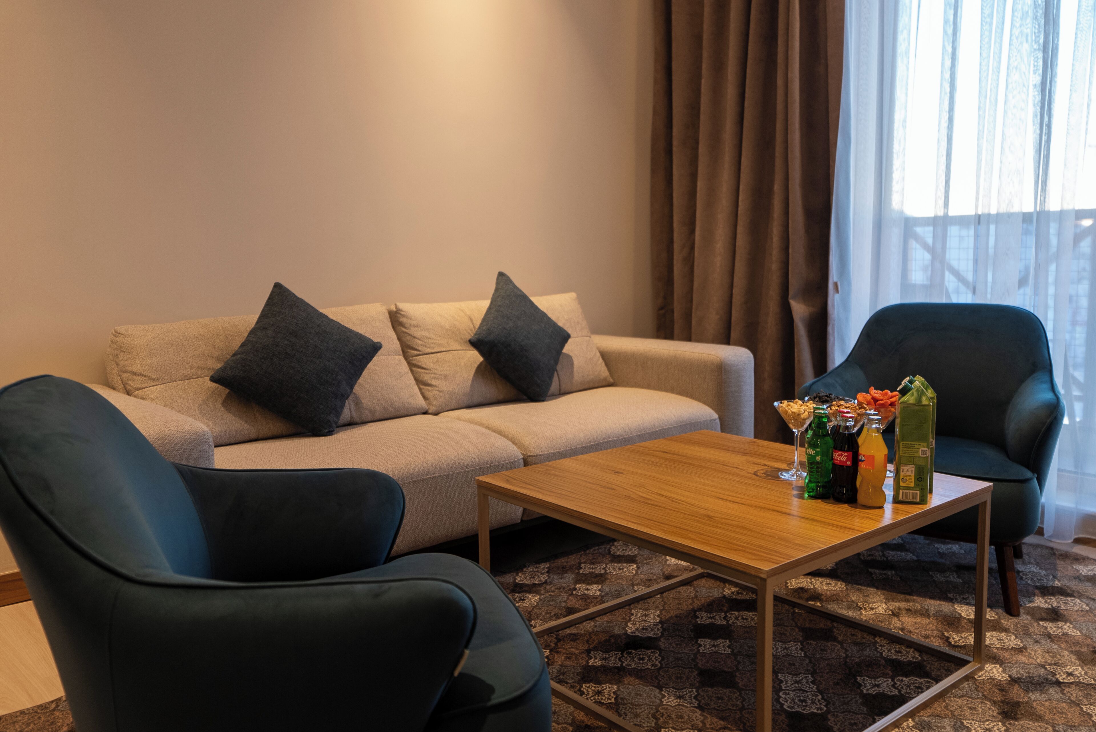 Una sala de estar con un sofá, dos sillones, una mesa de centro y un ventanal con cortinas.