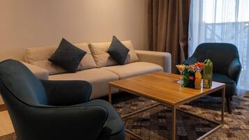 Una sala de estar con un sofá, dos sillones, una mesa de centro y un ventanal con cortinas.