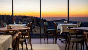 Un restaurante con mesas y sillas, vista al mar y un atardecer.