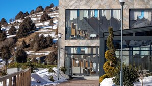 Un edificio moderno con amplios ventanales, una terraza de madera y un paisaje cubierto de nieve.