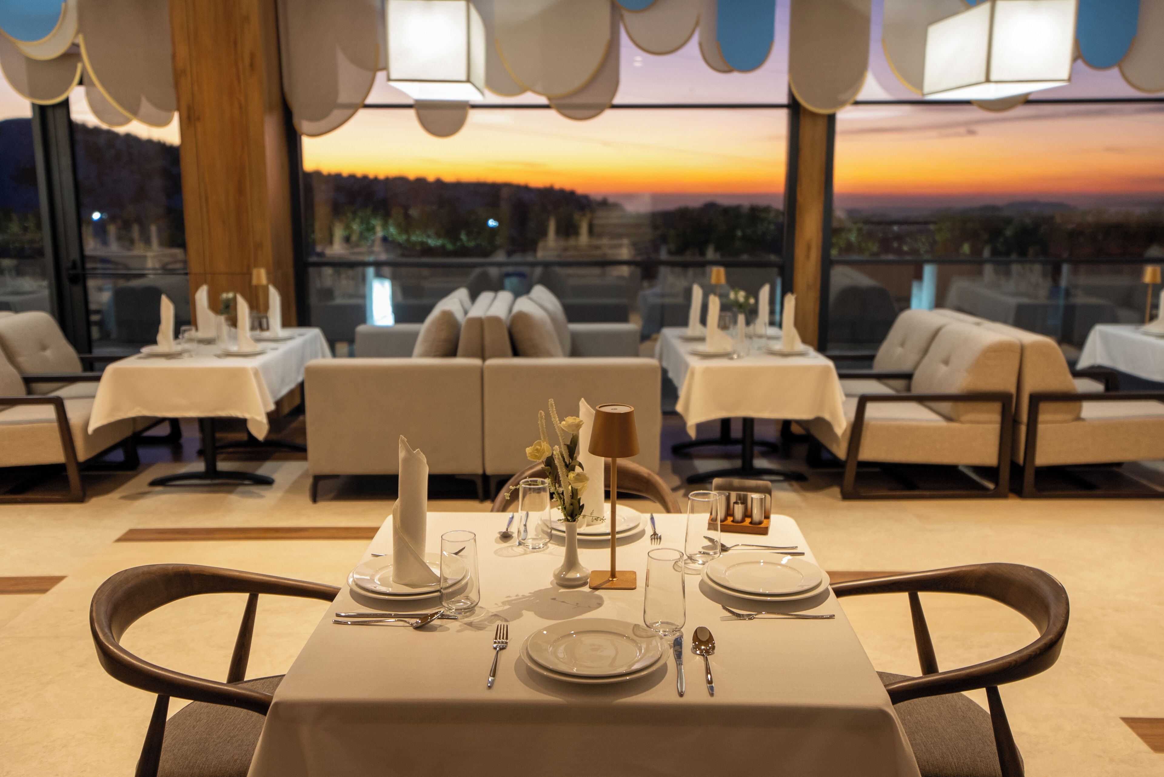 A restaurant with tables set for dining, a view of the sunset, and a modern interior design.