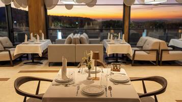 A restaurant with tables set for dining, a view of the sunset, and a modern interior design.