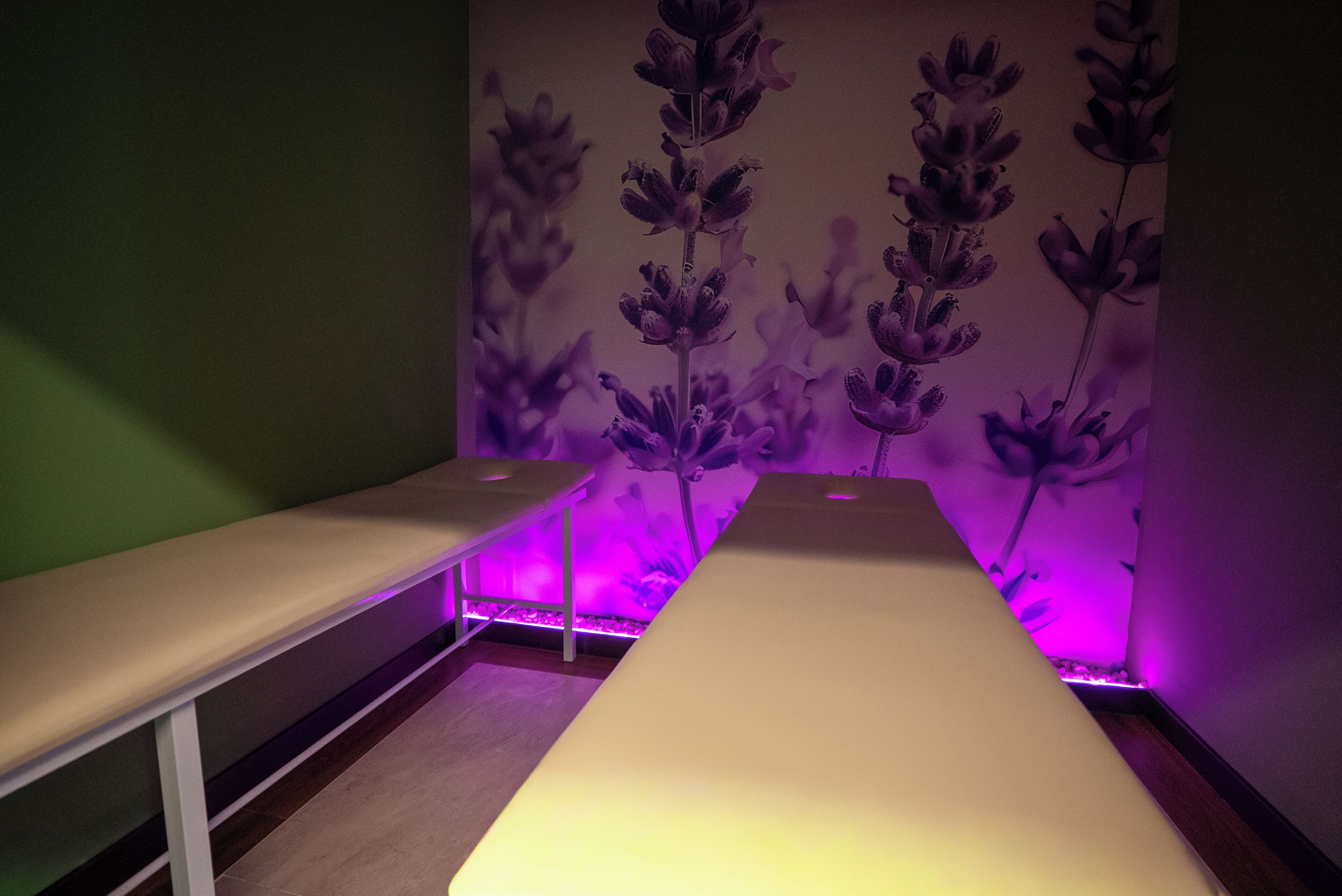Une pièce avec un lit long et étroit, un banc et un mur orné d’un motif floral.