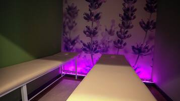 Une pièce avec un lit long et étroit, un banc et un mur orné d’un motif floral.