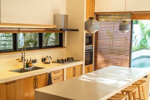 Une cuisine moderne dotée d’un îlot central, de meubles en bois, d’un four encastré et offrant une vue sur une piscine.