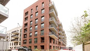 A multi-story residential building with balconies, a car parked in front, and a tree to the right. - Stratford Flat near ABBA Arena (London)