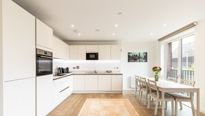 A modern kitchen with white cabinetry, a built-in oven, and a dining area with a table and chairs. - Stratford Flat near ABBA Arena (London)