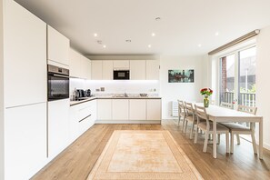 A modern kitchen with white cabinetry, a built-in oven, and a dining area with a table and chairs. - Stratford Flat near ABBA Arena (London)