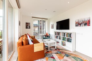 A modern living room with a sofa, a coffee table, a bookshelf, and a TV mounted on the wall. - Stratford Flat near ABBA Arena (London)
