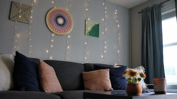 Uma sala de estar com sofá, adornos na parede, luzes de cordão e uma janela com cortinas.