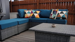 Um sofá modular com almofadas geométricas coloridas, uma mesa de centro trançada e um deck de madeira.