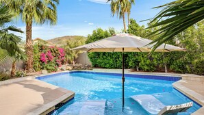 A swimming pool with a sun umbrella, lounge chairs, and surrounding greenery. - Bright Phoenix Oasis w/Private Pool & Mtn Views (Phoenix)