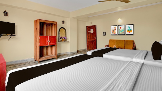 Une chambre d’hôtel avec deux lits, une armoire en bois, une télévision et un ventilateur de plafond.