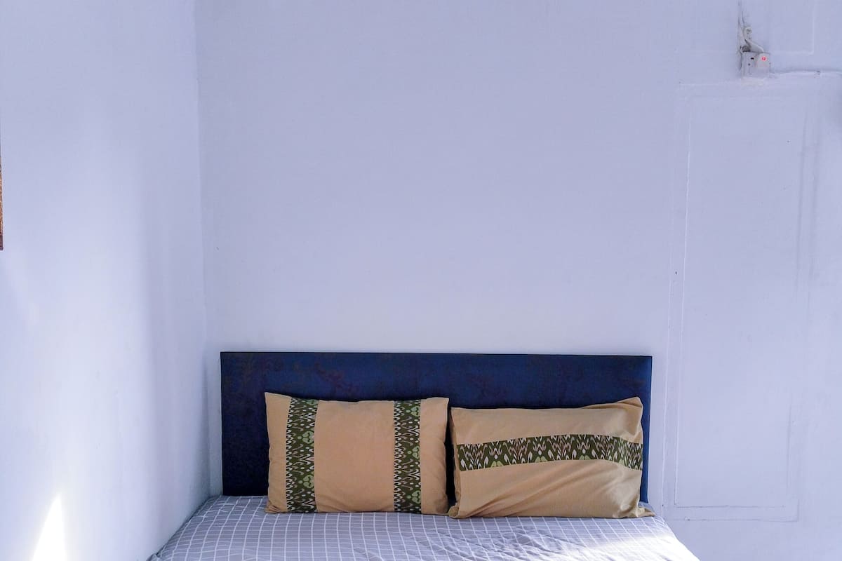 A single bed with a headboard, two pillows, and a rolled towel on a plain bedspread.