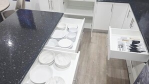 A kitchen with a black countertop, white cabinets, and a drawer with utensils.