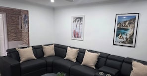 Un sofá modular negro con cojines color beige, una pared blanca con obras de arte enmarcadas y una puerta con textura similar a la piedra.