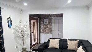A living room with a black sofa, two beige cushions, a potted plant, and a stone wall.