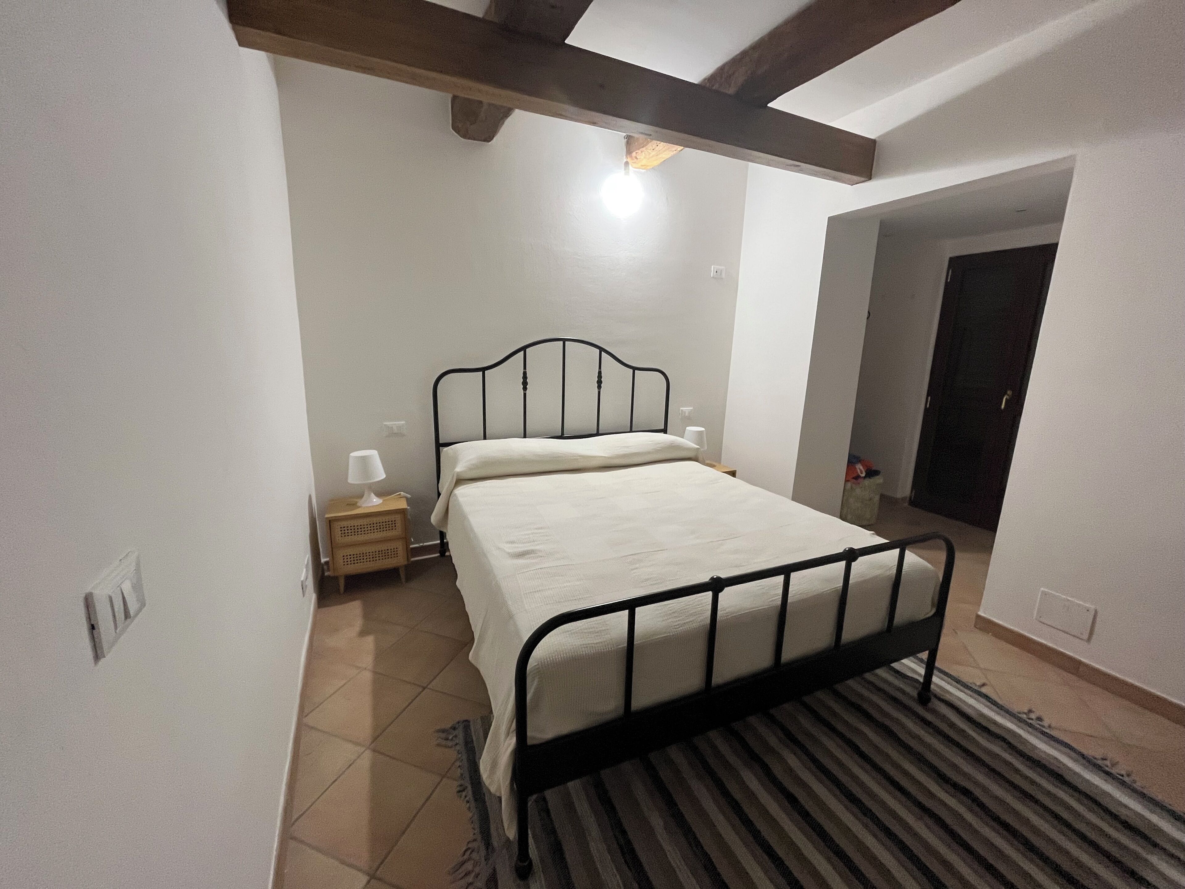 Una camera da letto con un letto, un comodino, una lampada e una porta che dà su un'altra stanza.
