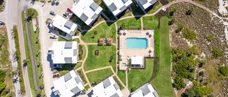 An aerial view of a residential area with multiple white houses, a swimming pool, and a tennis court.