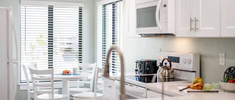 A modern kitchen with white cabinetry, a microwave, an oven, and a dining area with white chairs and a table.