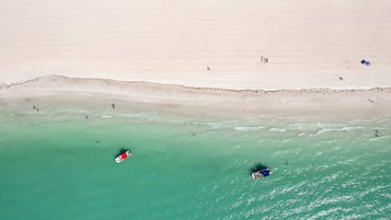 An aerial view of a beach with clear turquoise water, a sandy shore, and a few people and boats.