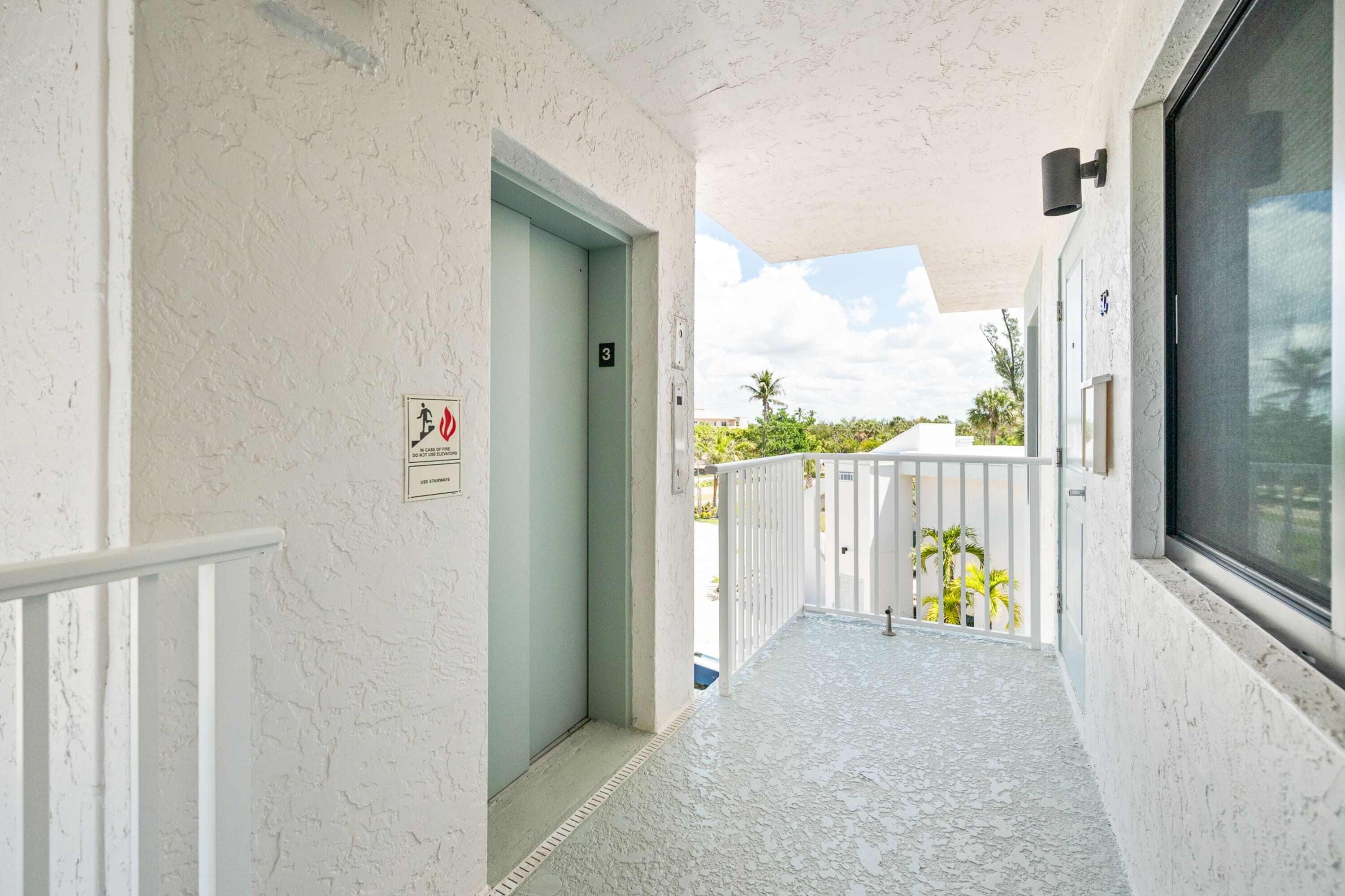 A corridor with a door, a balcony with a railing, and a window.