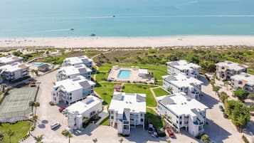A resort with multiple buildings, a swimming pool, tennis courts, and a beach view.
