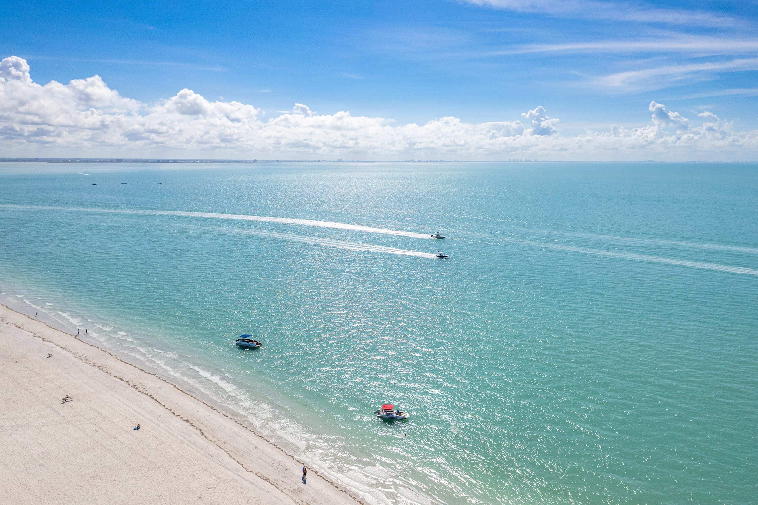 A beach with clear turquoise water, a sandy shore, and a few boats.