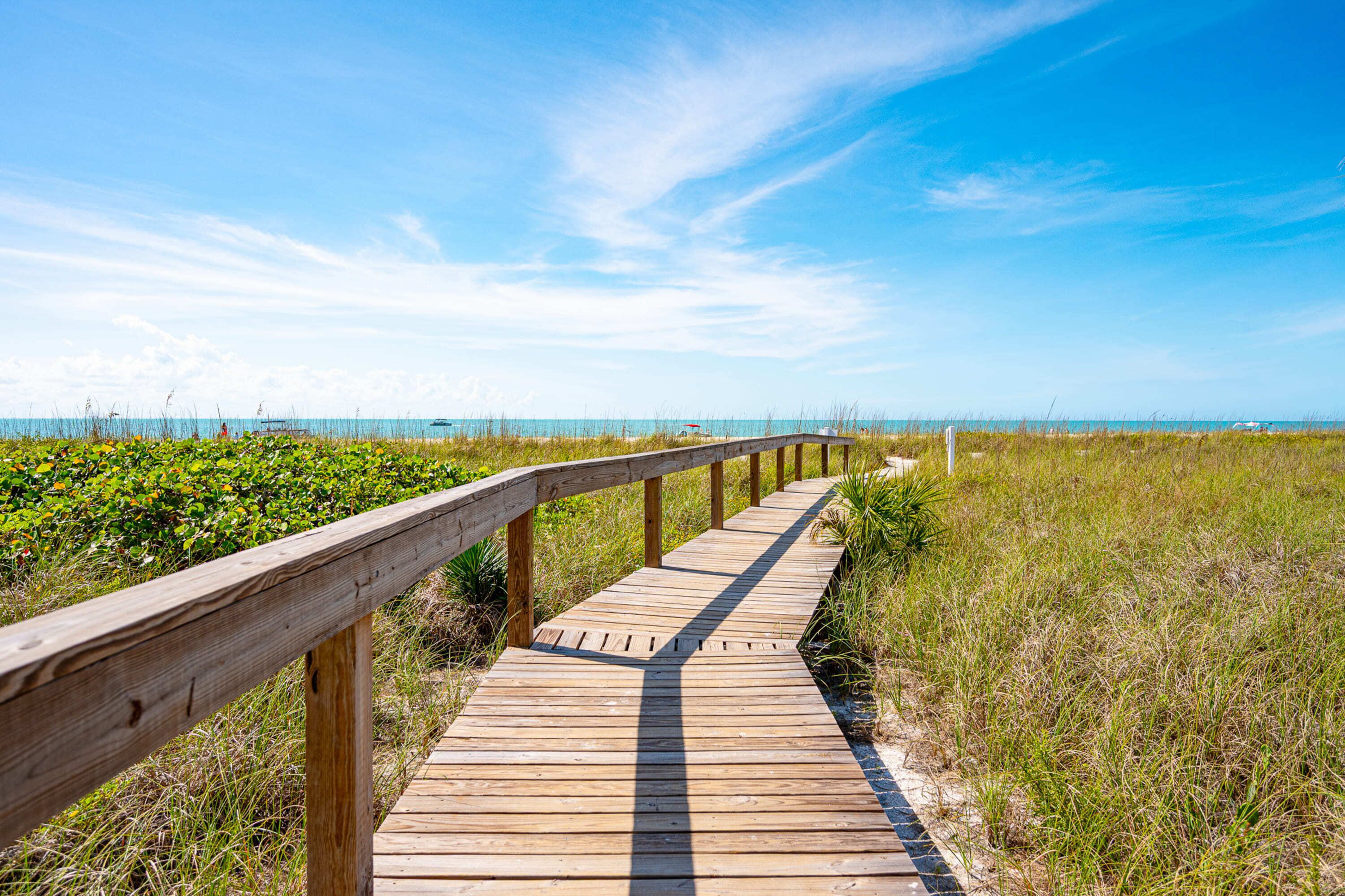 A wooden boardwalk leading to the beach, surrounded by grass and vegetation.